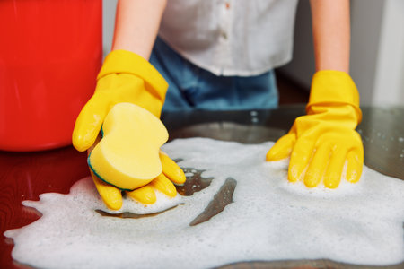 Woman in yellow rubber gloves cleaning a countertop with soap and sponge