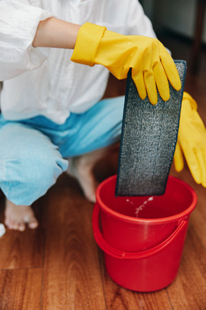 Person in rubber gloves cleaning floor with mop and bucket of water