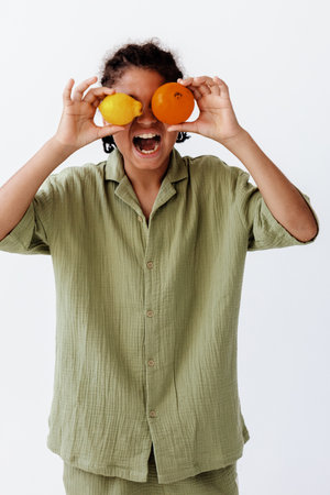 playful woman holding citrus fruits in front of her eyes with a trendy green shirtの写真素材