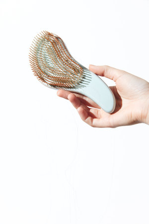 Hand holding a brush with a comb attached on a white background with hairbrush written on itの写真素材