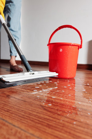 Woman cleaning hardwood floor with mop and bucket of water