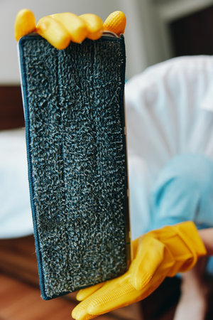 Person in yellow rubber gloves holding a black cloth in front of another person in white tshirt and yellow rubber gloves standing next to a bedの写真素材