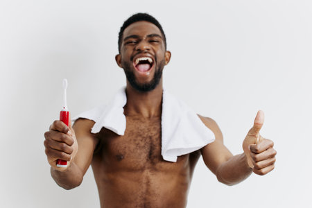 Healthy morning routine smiling shirtless man holding toothbrush and giving thumbs up for dental hygieneの写真素材