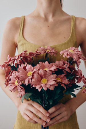 Woman in a yellow dress holding pink daisies with a smile on her faceの写真素材