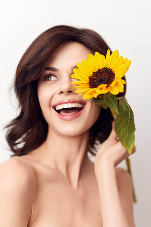 Smiling woman holding a sunflower in front of her face and looking at the cameraの写真素材