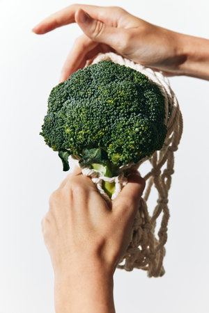 Person holding up broccoli in net bag on white background