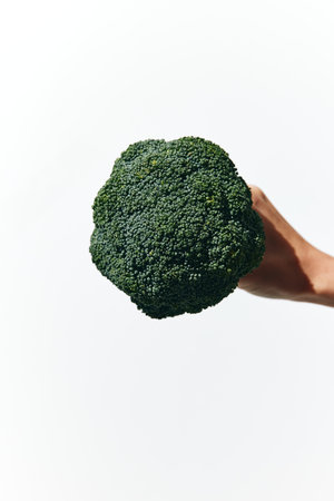 Person holding broccoli in front of a white background, with hand in the middle