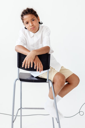 Young boy sitting on modern chair against blank white wall in minimalist room settingの写真素材