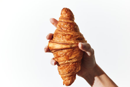 Person holding a large croissant in their left hand against white background