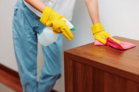 Cleaning concept woman in blue jeans and yellow rubber gloves cleans furniture with spray bottle and...