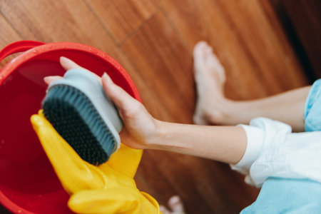 Person with rubber gloves cleaning wooden floor with brush and bucket of waterの写真素材