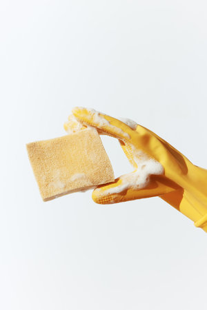 Person holding a piece of soap with a yellow rubber glove on a white surface, also holding a yellow sponge in the other handの写真素材