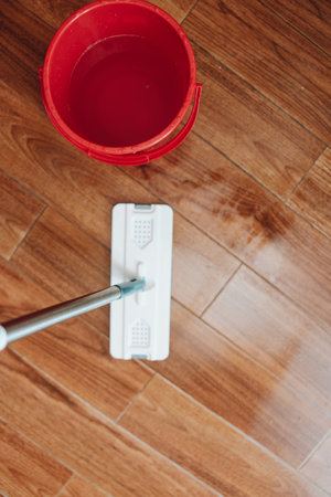 Person cleaning hardwood floor with mop and bucket of waterの写真素材