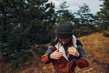 A young woman in a stylish hat and jacket standing on a serene dirt road in the peaceful woods,...