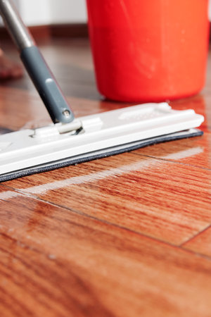 Woman cleaning hardwood floor with mop in front of bucket of water and red paintの写真素材