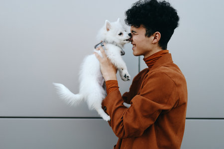 Young person holding a small white dog against a neutral gray background, sharing a playful momentの写真素材