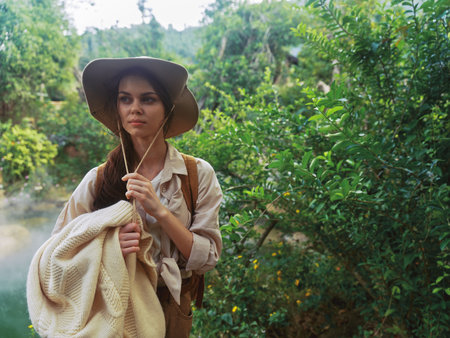 A woman wearing a hat and holding an umbrella in front of a river and treesの写真素材