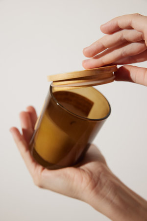 Person holding candle in glass jar with wooden lidの写真素材