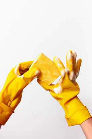 Two hands in yellow rubber gloves holding a soapcovered sponge on a white backgroundの写真素材