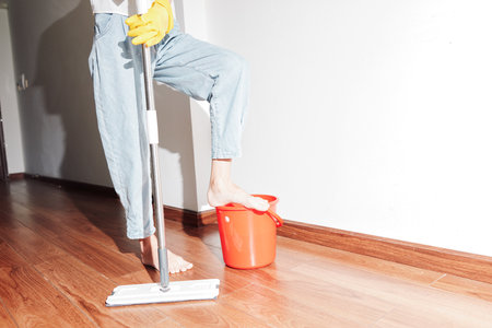 Woman cleaning wooden floor with bucket and mop nearby