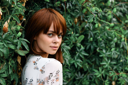 Vibrant redhaired woman standing in front of lush green plant wall