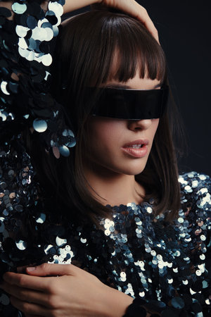A woman in a sequinned dress, with sunglasses on her head, poses confidently against a black...