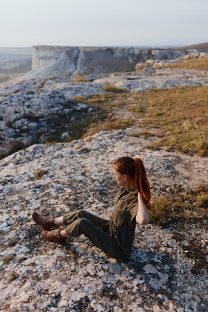 Woman sitting on a rock in the middle of a field, gazing at the horizon with a sense of wanderlust and adventureの写真素材