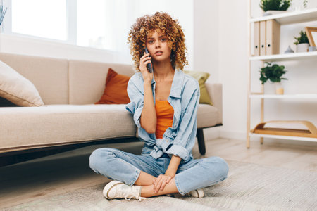 Happy Woman Holding Mobile Phone, Enjoying Online Games and Chatting in Cozy Living Roomの写真素材