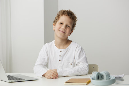 Smiling boy at home using laptop for elearning, immersed in a virtual world of education He sits at...