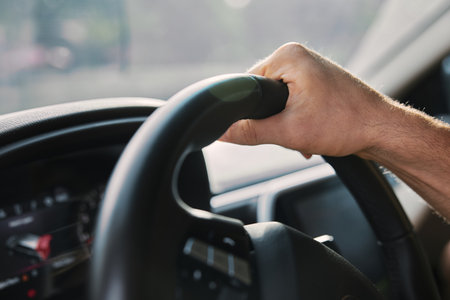 Close up of a hand gripping a steering wheel in a modern car with a blurred background The image...