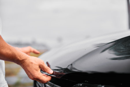 Car wrapping process with hands applying film on a black car surfaceの写真素材