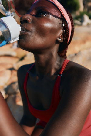 Close up of a woman drinking water, wearing a red athletic outfit and a headband, with a rocky...