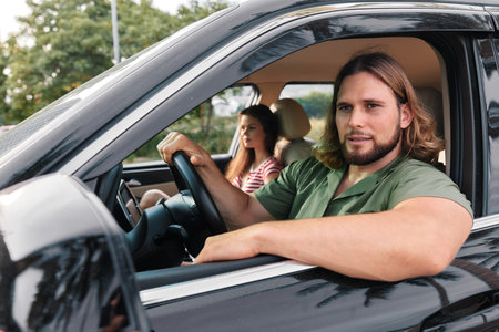 Young couple in a car during a casual drive, male driver with long hair and female passenger, both...