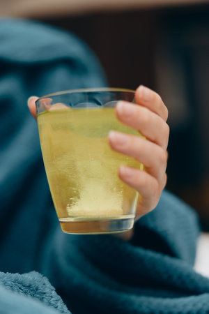 Woman in blue sweater drinking lemonade on a couch with a blanketの写真素材