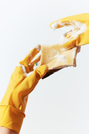 Pair of yellow rubber gloves holding up soap and sponge on white backgroundの写真素材