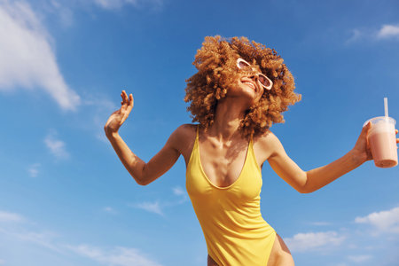 Joyful woman dancing on the beach in a yellow swimsuit against a bright blue sky