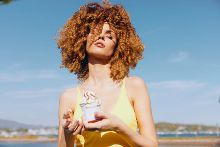 Young woman in a yellow dress holding ice cream against a sunny sky