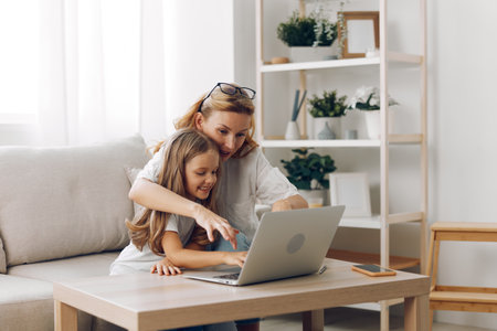 Mother and daughter bonding time on the couch while exploring a laptop together on a wooden coffee tableの写真素材