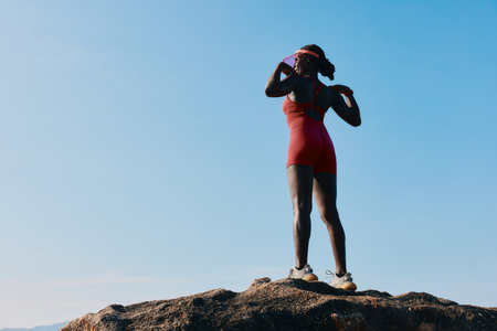 A confident athlete stands on a rocky peak, basking in the sun with a clear blue sky in the...