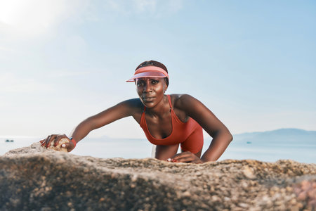 A woman in a bright orange swimsuit climbs on a rock by the beach, with a serene ocean backdrop The clear sky enhances the uplifting vibe of the sceneの写真素材