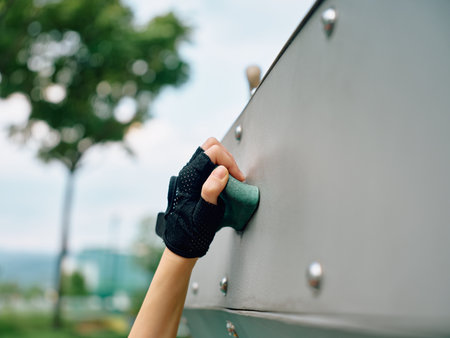 Close up of a climber s hand gripping a climbing hold on a grey rock surface, showcasing strength and determination against a blurred green backgroundの写真素材