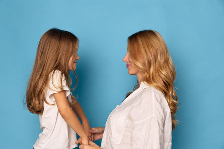 Mother and daughter holding hands against a blue background, smiling and connecting in a moment of joyの写真素材