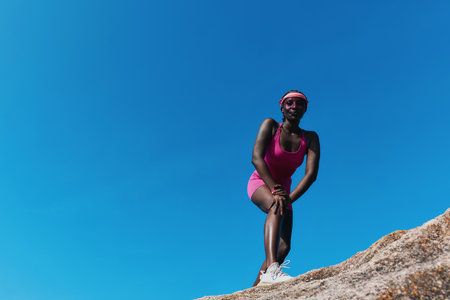 Confident woman in pink athletic wear posing on a rock against a clear blue skyの写真素材