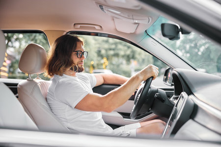 Man driving a car inside with a relaxed expression and sunglasses on, showcasing modern interior designの写真素材