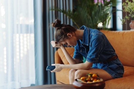 Worried woman sitting on couch with hands on head, looking at phone in front of her