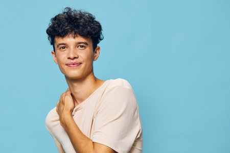 Young man smiling against a light blue background, wearing a casual beige shirt The photo captures a friendly, approachable demeanor and relaxed vibeの写真素材
