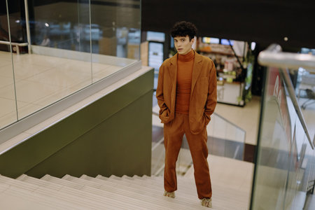Stylish young man in a brown suit stands on stairs in a modern interiorの写真素材