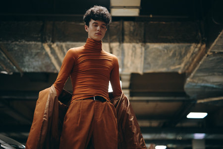 Stylish young man in an orange turtleneck and matching pants, posing confidently in a modern parking garageの写真素材
