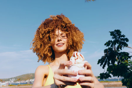 Young woman with curly hair enjoying ice cream under blue skyの写真素材