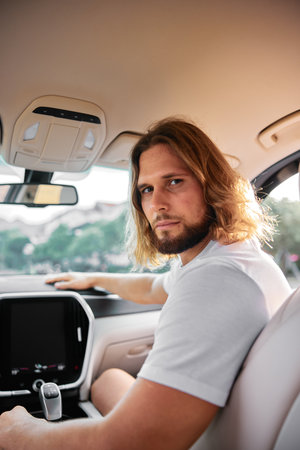 Young man with long hair sitting in car interior with thoughtful expression